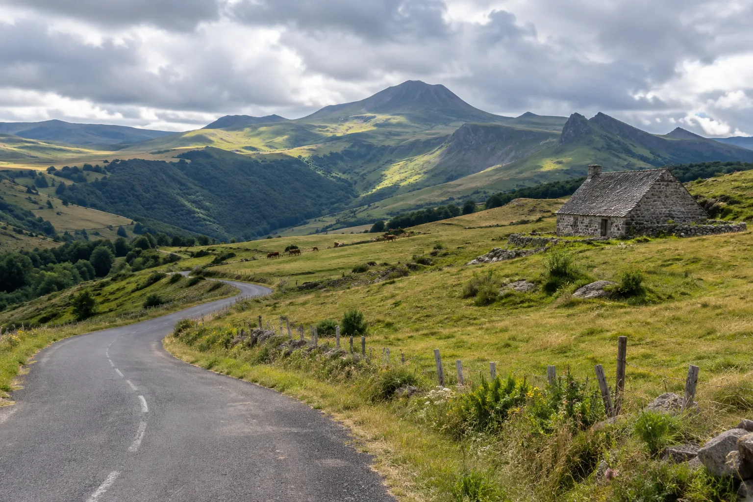 Une route traverse les pâturages du Cantal en direction des sommets volcaniques.